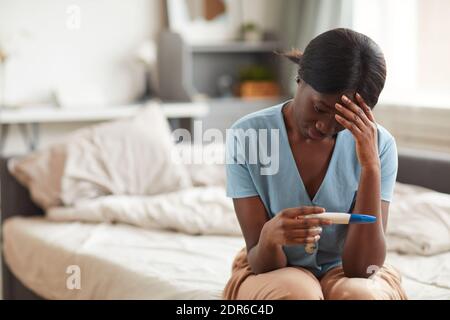 Ritratto della donna afro-americana preoccupata che guarda il test di gravidanza mentre si siede a letto a casa, copia spazio Foto Stock