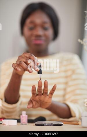 Primo piano di una giovane donna afroamericana che usa il nailpolish mentre fa manicure a casa, copia spazio Foto Stock