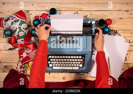 Atmosfera natalizia con una macchina da scrivere vintage, calze piene di dolci, una coperta rossa e un mucchio di fogli bianchi. Foto Stock