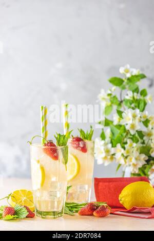 Bicchieri di bevanda rinfrescante ghiacciata con limone e fragola serviti su un tavolo rosa chiaro. Cocktail freschi con frutta ghiacciata e decorazioni alle erbe Foto Stock