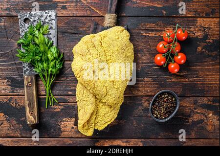 Greggia grande schnitzel viennese su un tagliere. Sfondo di legno nero. Vista dall'alto. Foto Stock