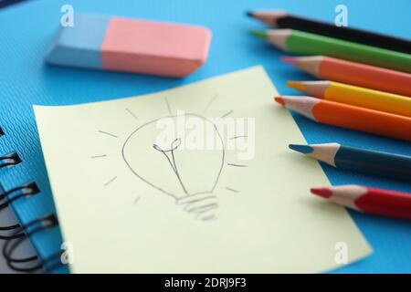 Su un foglio di carta bianco, la lampadina viene disegnata accanto a matite e adesivi colorati Foto Stock