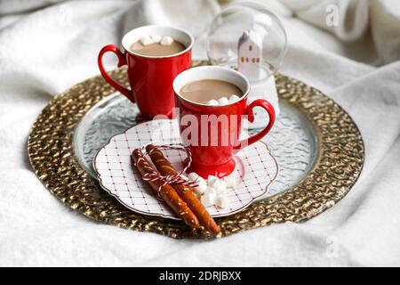 Un set natalizio con due tazze di cioccolata calda con marshmallow, pretzel e un globo di neve Foto Stock