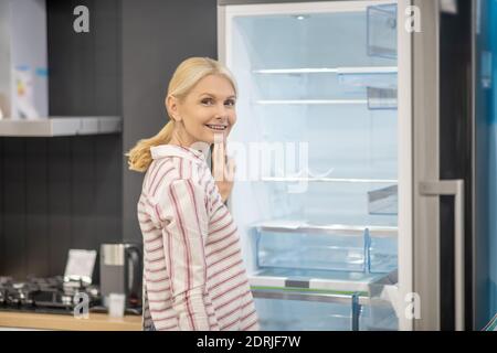 Donna in camicia a righe che sceglie il frigorifero in uno showroom Foto Stock