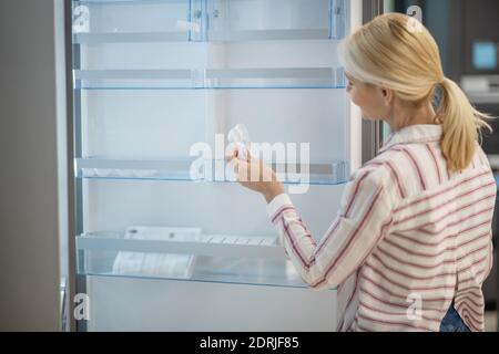 Donna in camicia a righe che sceglie il frigorifero in uno showroom Foto Stock