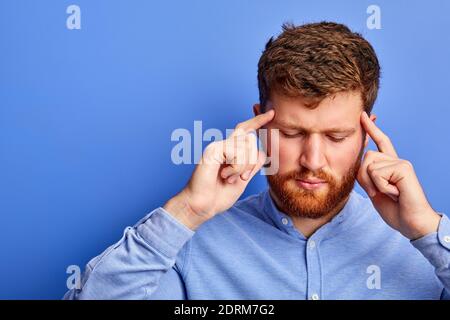 ritratto di pensieroso ragazzo caucasico pensando isolato su sfondo blu, stare con gli occhi chiusi, tenendo la testa, concentrato sui pensieri Foto Stock