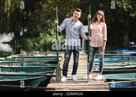 giovane coppia innamorato divertirsi con i remi sul ponte di legno. donna e uomo alla moda godersi la canoa sul lago soleggiato Foto Stock