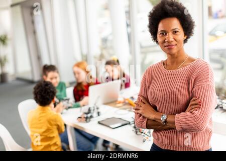 Smily African American insegnante di scienza femminile con gruppo di bambini programmazione di giocattoli e robot elettrici in classe robotica Foto Stock