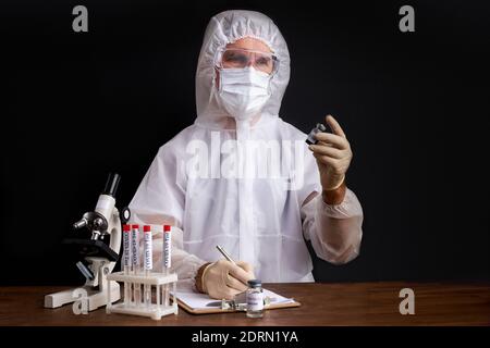 Lo scienziato maschile sta testando un campione di provette biologiche contaminate da Corona-virus Covid 19, utilizzando il microscopio Foto Stock