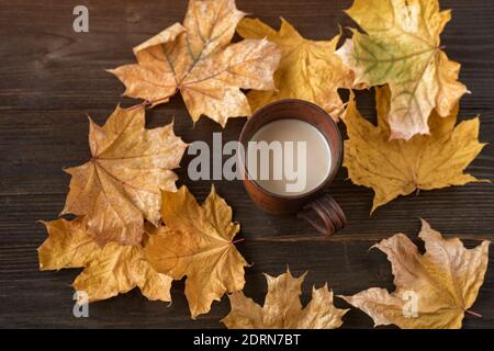 Tazza di cacao caldo su sfondo di legno tra foglie d'autunno. Caffè con latte e foglie d'autunno. Foto Stock