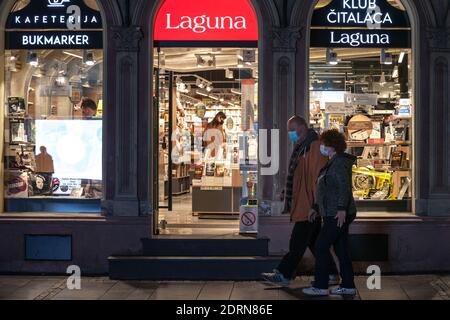 BELGRADO, SERBIA - 21 OTTOBRE 2020: Coppia anziana che passa davanti ad una libreria con i clienti che scelgono libri che indossano una maschera respiratoria Foto Stock