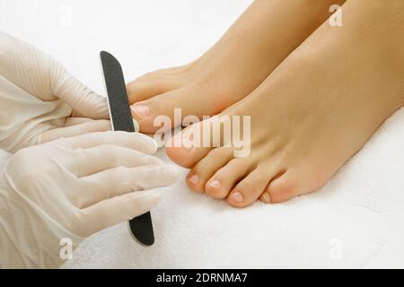 Pedicure master durante il lavoro. Primo piano di piedi femminili e mani in guanti con una lima per unghie. Foto Stock