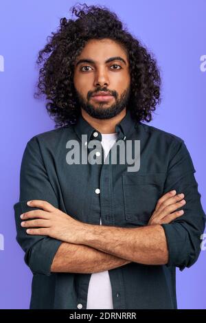 ragazzo arabo che si pone con sicurezza guardando la macchina fotografica, giovane uomo con la pelle scura in studio, in piedi con le braccia incrociate Foto Stock