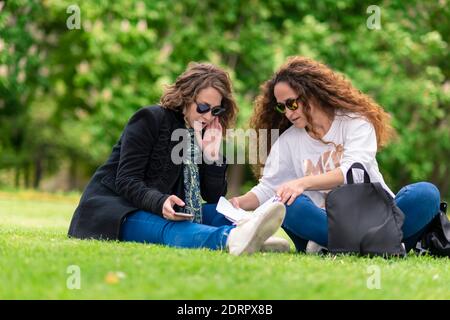 Parlare e studiare, con il telefono, rilassati nel parco, seduto sull'erba. Foto Stock