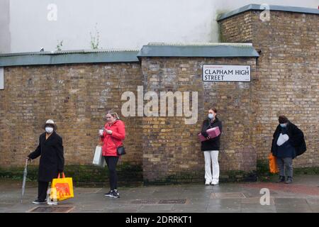 Clapham, Londra, 21 dicembre 2020: Le persone formano una coda socialmente distanziata presso l'Ufficio postale di Clapham. Molte persone nel livello 4 non sono più in grado di visitare i parenti o di formare una bolla sociale di Natale e così sarà l'invio di pacchi di regali a persone care. Anna Watson/Alamy Live News Foto Stock