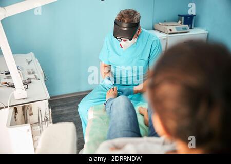 Chiropodist professionale che tratta i piedi durante la procedura medica Foto Stock