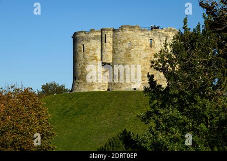 I visitatori su alti bastioni della Torre di Clifford sotto il cielo blu e il sole - rovine del castello storico in cima alla collina e punto di riferimento a York, North Yorkshire, Inghilterra, Regno Unito. Foto Stock