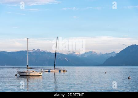 Lago alpino con la calma acqua blu con due barche ormeggiate circondato da cime innevate. Montreux nel lago di Ginevra Foto Stock