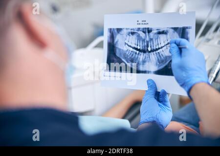 Chirurgo maschile con radiografia della mascella del paziente in ufficio Foto Stock