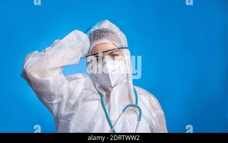 Ritratto di donna stanca che indossa tuta protettiva per combattere il coronavirus pandemia covid-2019. Ritratto medico su sfondo blu Foto Stock