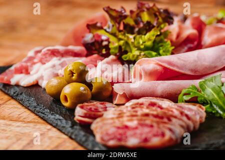 Piatto di salsiccia. Vari tipi assortiti di salsicce con olive su un piatto nero su un tavolo di legno. Diversi tipi assortiti di salsicce spagnole. Foto Stock