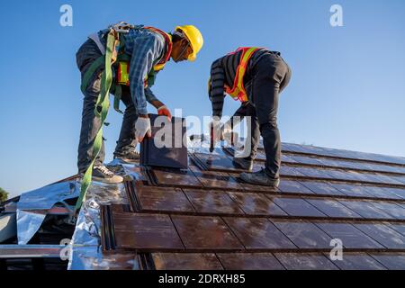 I lavoratori addetti alla costruzione installano un nuovo tetto in piastrelle di ceramica nel cantiere. Foto Stock