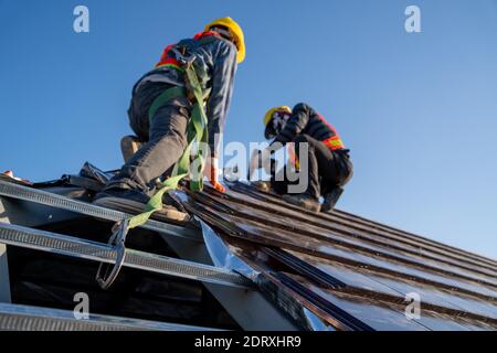 Lavoratori edili che indossano la cintura di sicurezza dell'attrezzatura ad altezza durante il lavoro Installare il nuovo tetto in piastrelle di ceramica dell'edificio con gli attrezzi per tetti elettrico Foto Stock