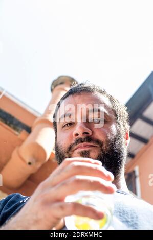 primo piano di un ragazzo con barba nera e cocktail, sparando dal basso Foto Stock