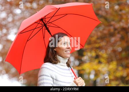 Donna adulta felice sotto ombrello rosso contemplando viste in autunno in un parco Foto Stock