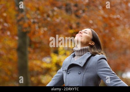 Donna di media età che indossa una giacca grigia che respira aria fresca in piedi in una foresta nella stagione di autunno Foto Stock