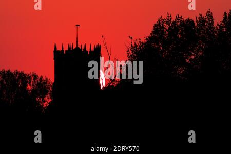 Silhouette del 15 ° secolo Torre di Christchurch Priory, Regno Unito, contro il cielo rosso arancione di UN tramonto Foto Stock