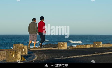 CAPE TOWN, SUDAFRICA - 21 dicembre 2020: Una coppia che si prende una passeggiata nella mattina presto con il mare sullo sfondo Foto Stock