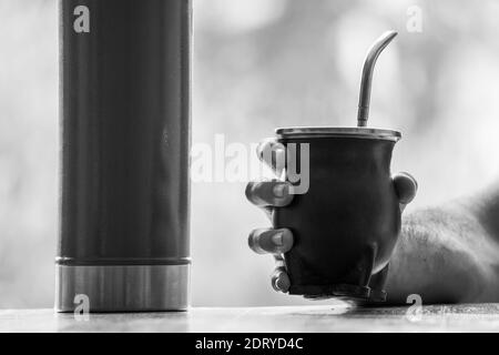 Scala di grigi fuoco selettiva di una mano che tiene un calabash accoppiare la coppa con la paglia Foto Stock