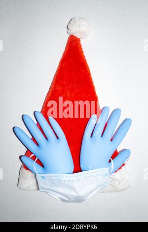 Cappello di Natale con maschera chirurgica e un paio di guanti medici in vinile gonfiato blu. Vista dall'alto Foto Stock