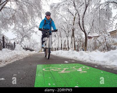Il ragazzo si muove su una bicicletta in inverno lungo la pista ciclabile. Modalità di trasporto urbano ecocompatibile Foto Stock