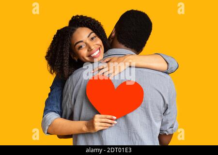 Felice donna afroamericana in amore abbracciando il ragazzo e la tenuta cuore rosso Foto Stock