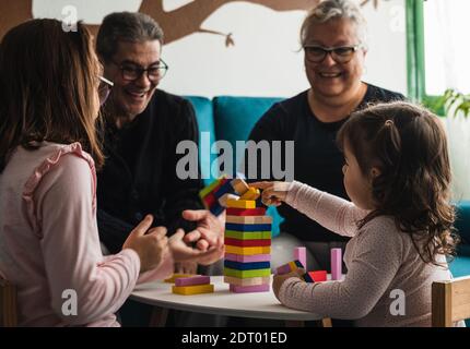 Nonna e nonno giocano un gioco da tavolo con le loro due nipoti, tutte caucasiche, seduti in soggiorno, sorridendo mentre hanno un grea Foto Stock