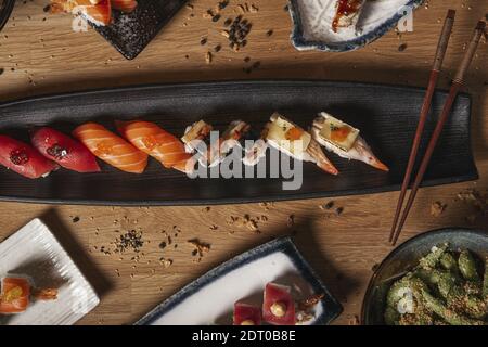 Una vista dall'alto di una varietà di sushi, nigiri, sashimi, yakisoba ed edamame su un tavolo di legno del ristorante Foto Stock