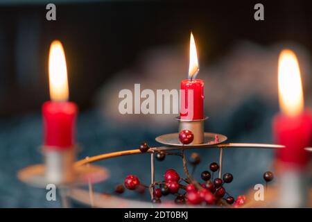 Candele rosse che bruciano su una corona di Avvento autofatta fatta di filo griglia decorata con bacche rosse secche con divano sfocato camera sullo sfondo Foto Stock