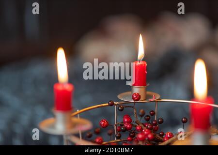 Candele rosse che bruciano su una corona di Avvento autofatta fatta di filo griglia decorata con bacche rosse secche con divano sfocato camera sullo sfondo Foto Stock