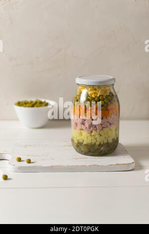Ingredienti per l'insalata russa Olivier in un vasetto di vetro su fondo bianco. Cucina russa. Spazio di copia. Foto Stock
