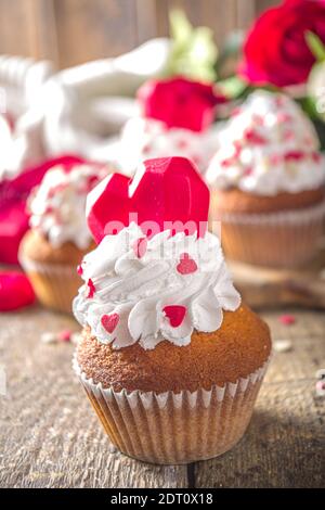 Cupcake con cuore per San Valentino. San Valentino dolce Dessert, cupcake alla vaniglia con panna montata alla vaniglia e zucchero rosso cuore decorazione per San Valentino Foto Stock