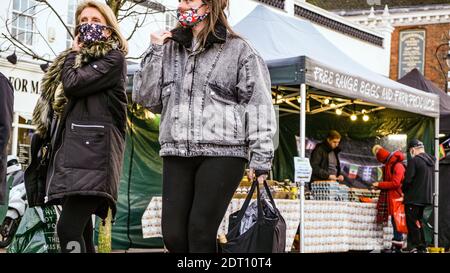 Madre e figlia che indossano maschere facciali di protezione camminando attraverso UN Mercato che trasporta il loro shopping Foto Stock