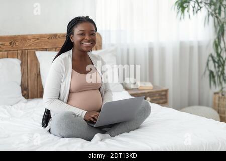 Offerte di lavoro online per donne incinte. Black expectant Mamma che usa il notebook a casa Foto Stock