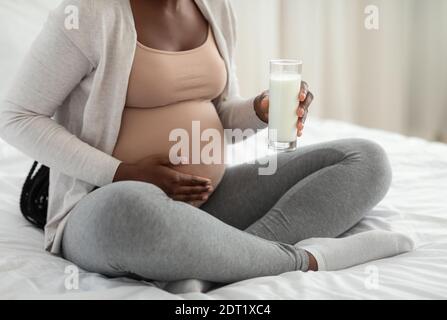 Nutrienti di gravidanza. Donna incinta nera vetro di tenuta con latte, poggiato sul letto Foto Stock