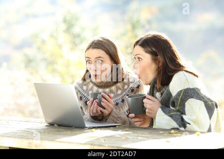 Sorpresi gli amici in inverno che controllano il portatile seduto in una panca Foto Stock