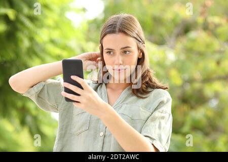 Donna che pettina i capelli usando lo smartphone come specchio in un parcheggio Foto Stock