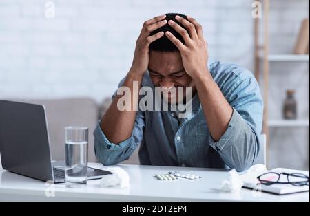 Black Man che soffre di mal di testa che tocca testa seduta sul luogo di lavoro Foto Stock
