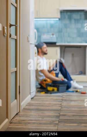 Colpo sfocato di riparatore professionista con cassetta degli attrezzi che prende una pausa, seduto sul pavimento all'interno Foto Stock