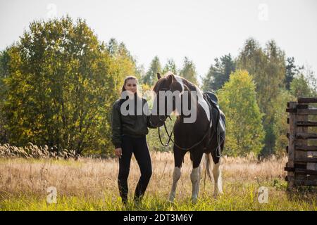 Una giovane ragazza conduce il suo cavallo dalla briglia lungo un percorso lungo la recinzione. Foto Stock